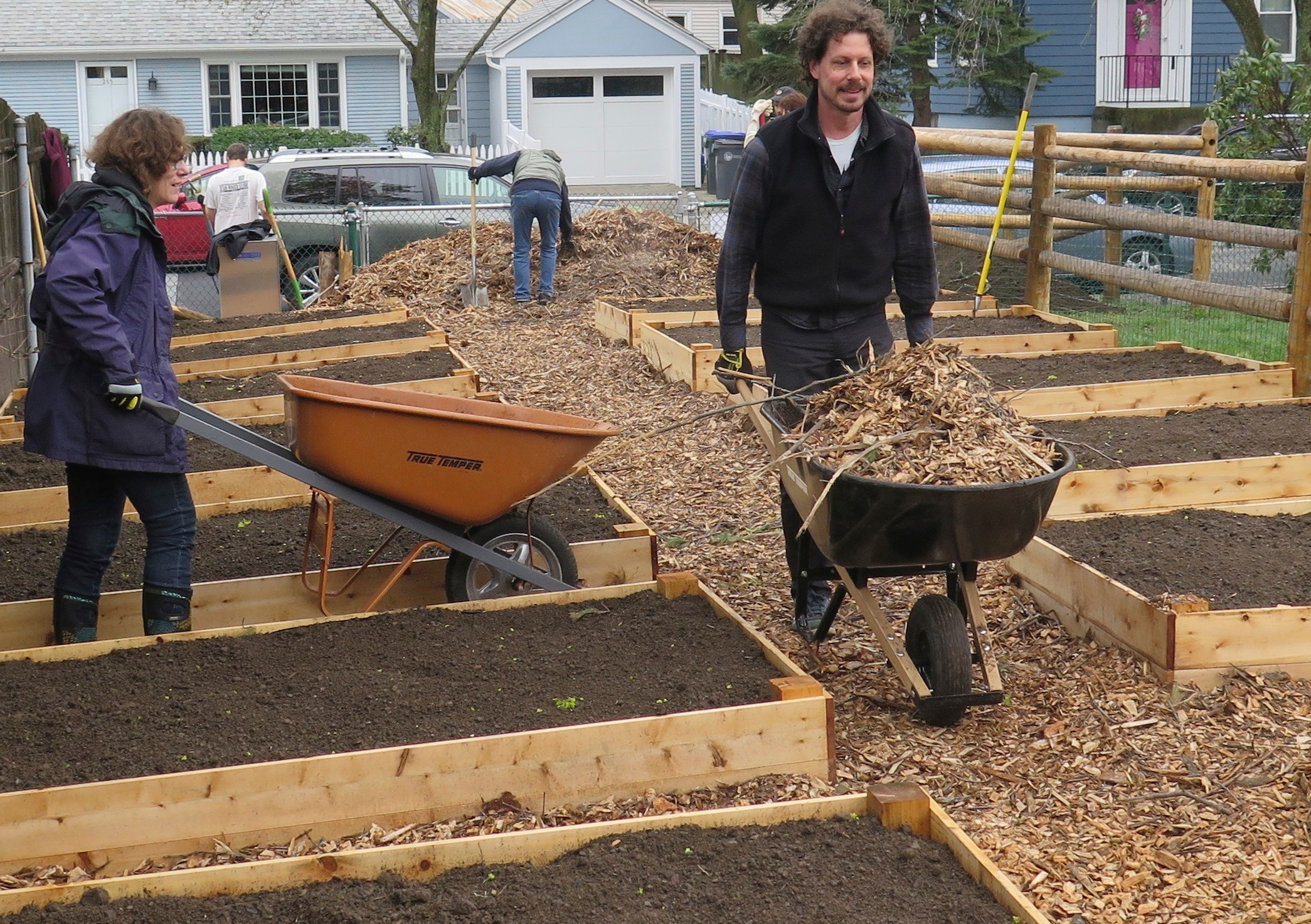 Wheelbarrows and muscles spread mulch between the raised beds of the Summit Neighborhood Community Gardens on April 22, Earth Day.